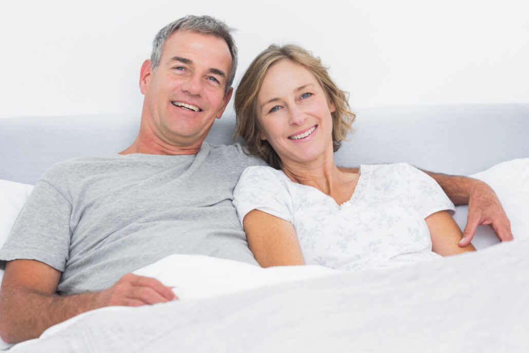Pareja feliz y relajada en la cama tras una noche de buen descanso, libre de ronquidos.